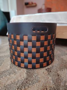 a brown and black leather basket sitting on top of a table next to a bed