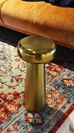 a gold stool sitting on top of a rug in front of a brown bench with an orange cushion