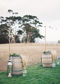 an outdoor ceremony setup with two barrels and candles on the grass, surrounded by string lights