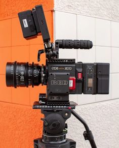 a video camera attached to a tripod in front of an orange brick wall and white tile