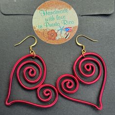 two red heart shaped wire earrings sitting on top of a gray table next to a sticker