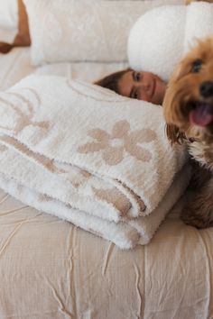 a dog laying on top of a bed next to a woman with her head under a blanket