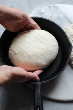 a person holding a ball of dough in a skillet on top of a counter