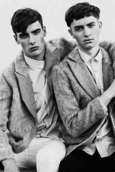 two young men sitting next to each other wearing coats and ties on their lapels