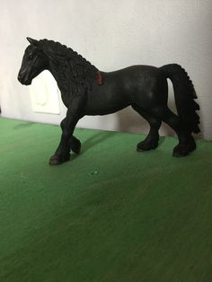 a black toy horse standing on top of a green floor next to a white wall