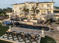 an outdoor swimming pool with lounge chairs and palm trees in front of a large mansion