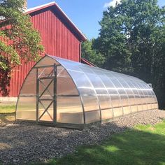 a large metal greenhouse in front of a red barn with trees and grass around it