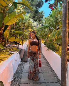 a woman walking down a sidewalk next to trees and plants on either side of her