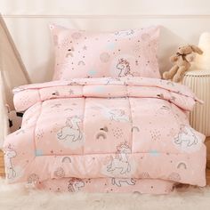 a pink bed set with unicorns and stars on the comforter, next to a teddy bear