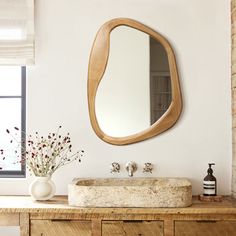 a bathroom with a sink, mirror and vase on top of the counter in front of a window