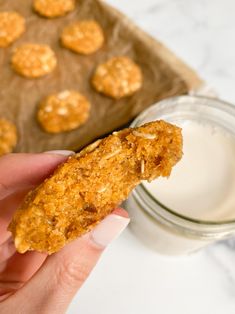 a person holding up a cracker with some food on it and a glass of milk in the background