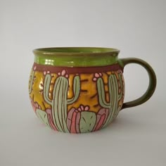 a green and yellow ceramic mug with cactus designs on the outside, sitting on a white surface