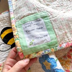 a person is holding up a quilt with a bee on it and the name of their baby