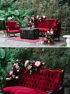 a red velvet couch sitting in front of a stone wall with greenery and flowers on it