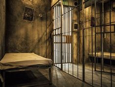 a jail cell with a mattress and bars on the wall, in front of a door