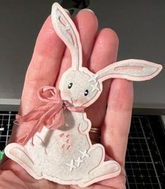 a hand holding a small white rabbit with a pink bow