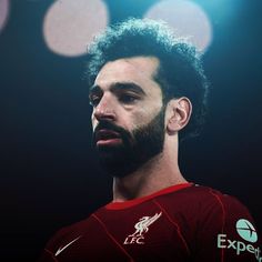 a bearded man wearing a red shirt and looking off into the distance with lights in the background