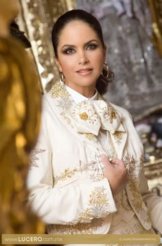 a woman wearing a white jacket and black pants standing in front of some gold decorations