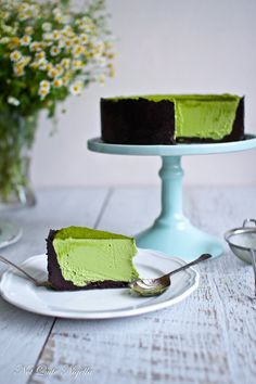 a piece of green cake on a plate with a fork and flowers in the background