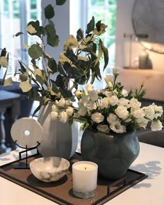 a vase with white flowers on a tray next to a candle