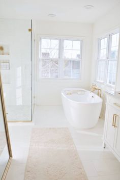 a large white bathtub sitting next to a window in a bathroom with a rug on the floor