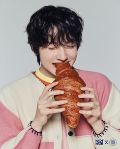 a young man eating a croissant while wearing a pink and white striped sweater