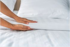 two hands on top of a bed with white sheets and pillow cases in front of them