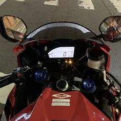 a red motorcycle parked on the side of a road next to a crosswalk with two mirrors