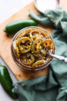 a jar filled with pickles on top of a cutting board next to green peppers