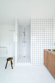 a white tiled bathroom with a stool and sink in the corner, next to a walk - in shower