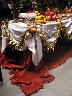 a table covered with fruit and silverware on top of a red cloth draped over it