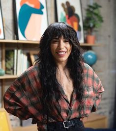 a woman with long black hair standing in front of some art on the wall behind her