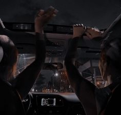 two people sitting in the back seat of a car with their hands up to the ceiling