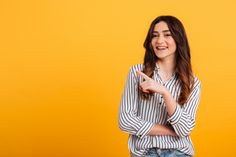 a young woman is smiling and pointing to the side with her finger on an orange background