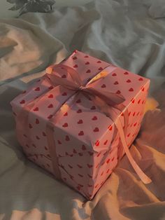 a pink gift box with red hearts on it sitting on a white sheet covered bed