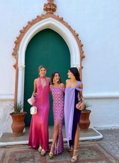 three beautiful women standing next to each other in front of a green door wearing dresses