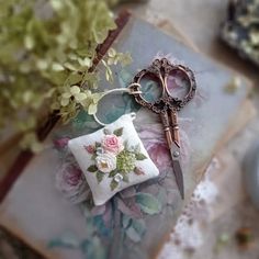 a pair of scissors sitting on top of a pillow next to a flower pot with flowers in it