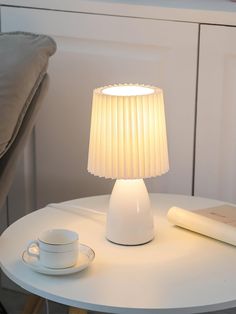 a white table with a lamp on it next to a remote control and coffee cup