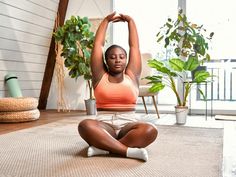 a woman sitting on the floor in front of a potted plant and stretching her arms