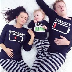 a man and woman laying on top of a bed with two babys wearing matching shirts