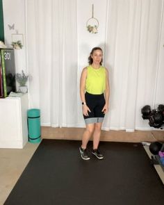 a woman standing in front of a black mat on top of a floor next to a white curtain