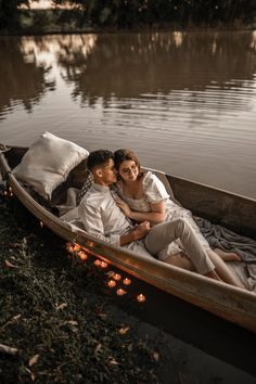 a man and woman are sitting in a boat on the water with candles around them