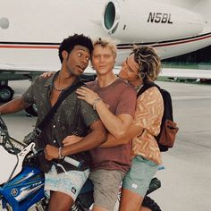 three people on a motorcycle with an airplane in the background