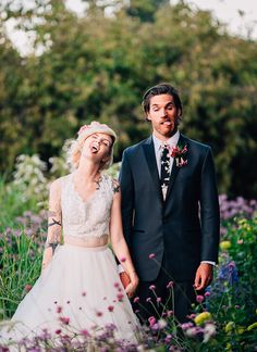 a man and woman standing next to each other in a field full of purple flowers