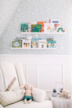 a white chair with a stuffed animal on it in front of a wall mounted book shelf