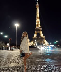 a woman standing in front of the eiffel tower at night