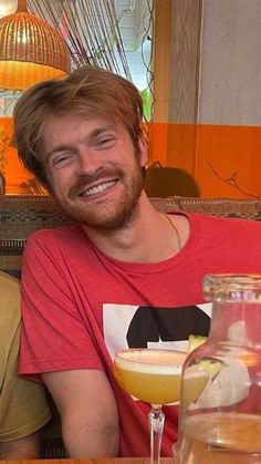 two men are sitting at a table with drinks in front of them and one is smiling