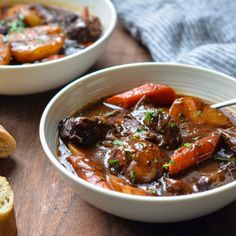 two bowls of beef stew with bread on the side