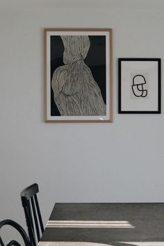 two framed pictures hang on the wall above a dining room table with chairs and a black chair