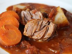 some meat and carrots are on a plate with gravy in the middle